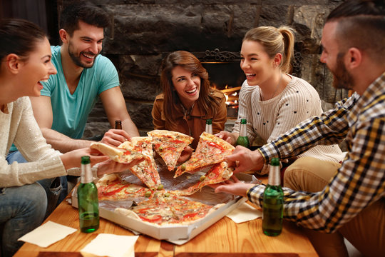 Group of young people taking pieces of big family pizza