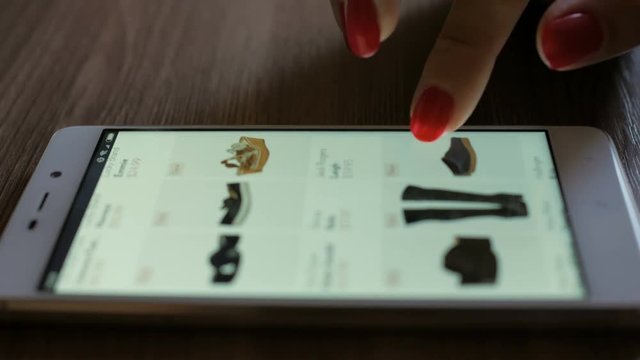 Woman looks at the goods in the online shoes store. People using Smartphone, online shopping. Close-up. 4K UHD. Screen is blurred.