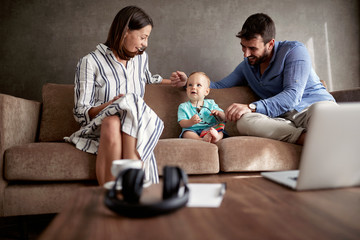 Happy mom and dad with their baby boy playing and reading book at home.