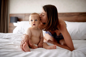 Fototapeta na wymiar Happy loving family. Mother kissing her child son on the bed.