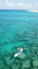 Aerial drone photo of couple practicing Stand Up Paddle or SUP in tropical exotic emerald and sapphire island sea