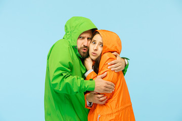 The young couple posing at studio in autumn jacket isolated on blue. Human negative emotions. Concept of the cold weather. Female and male fashion concepts