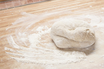 Whole wheat pizza dough shaped into ball on floured wooden background