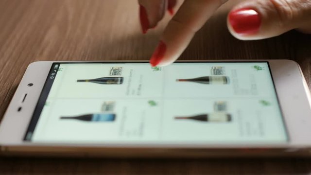Woman orders red wine home in an online store. Female selects the alcohol in the grocery online store. Close-up. 4K UHD. Screen is blurred.