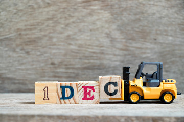 Toy forklift hold block c to complete word 1dec on wood background (Concept for calendar date 1 in...