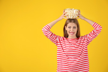 Beautiful young woman with bowl of popcorn on color background