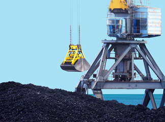 Working port crane and bucket, loading of coal. Marine loading terminal, trading port.  Grapple crane and pile of hard coal against the sea and blue sky
