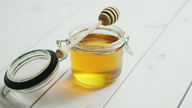 Glass jar full of honey with spindle on white wooden background