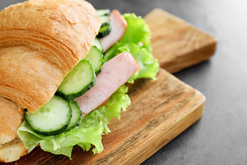 Wooden board with tasty croissant sandwich on grey table