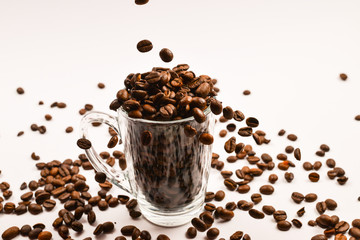 Grains of coffee are poured into a glass cup on a white background