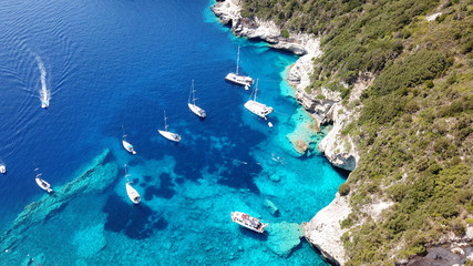 Aerial drone bird's eye view photo of sail boats docked in tropical caribbean paradise bay with white rock caves and turquoise clear sea