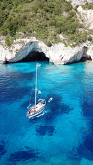 Aerial drone bird's eye view photo of sail boats docked in tropical caribbean paradise bay with white rock caves and turquoise clear sea