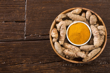 Turmeric powder and fresh turmeric on wooden background