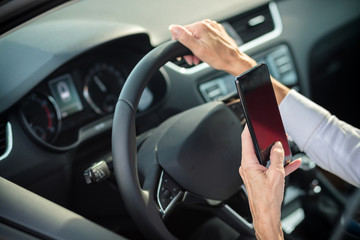 Mature woman using a smart phone while driving a car. Rear angle view through side window