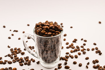 Grains of coffee are poured into a glass cup on a white background