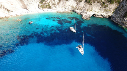 Aerial drone bird's eye view photo of sail boats docked in tropical caribbean paradise bay with white rock caves and turquoise clear sea