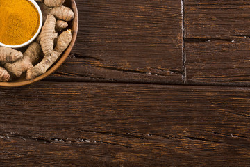 Turmeric powder and fresh turmeric on wooden background