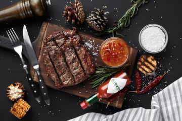 Medium rare grilled Steak Ribeye with corn and garlic on serving board block on black background