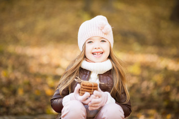 Little girl in pink hat and leather jacket in the autumn with cookies in her hands smiling close-up