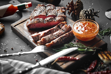 Grilled Steak cut in pieces decorated with seasoning and oil on black background. Top View. Copy...