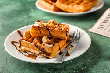 Delicious waffles with banana slices and chocolate sauce on color table