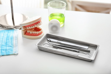 Tray with dentist's tools, mask and artificial jaw on light table in doctor's office