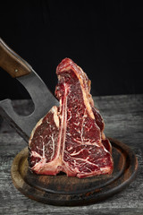 Fresh raw t-bones steak on an olive wooden board with sea salt and a kitchen ax.