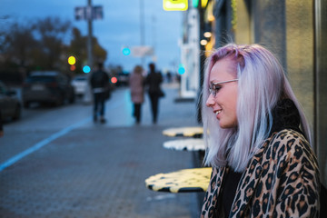 Fashionable blonde girl with glasses in leopard coat sitting in