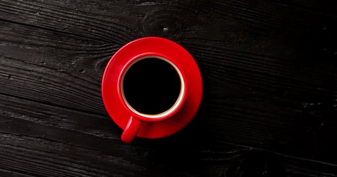 From above view of red cup of coffee with saucer on wooden background 