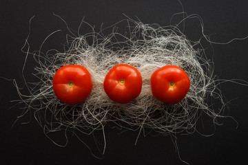 Three red tomatoes on a dark background with white fibers