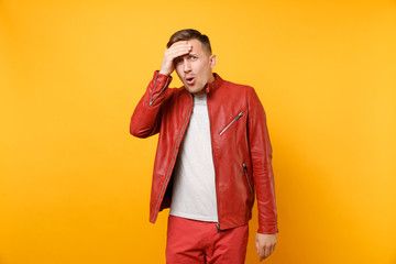 Portrait vogue shocked handsome young man 25-30 years in red leather jacket, t-shirt standing isolated on bright trending yellow background. People sincere emotions lifestyle concept. Advertising area