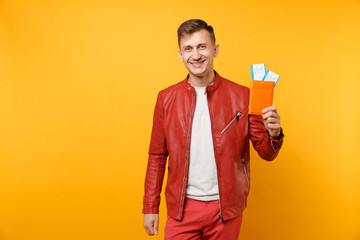 Portrait vogue smiling handsome young man in red leather jacket t-shirt hold passport tickets isolated on bright trending yellow background. People sincere emotions lifestyle concept. Advertising area