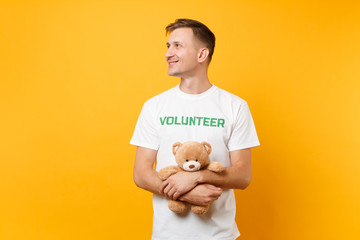 Portrait of good man in white t-shirt with written inscription green title volunteer hold teddy...