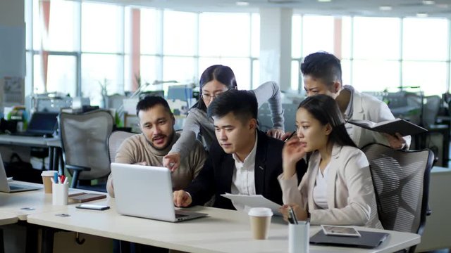 Medium shot of five Asian businesspeople looking at laptop computer screen and getting upset because of failure