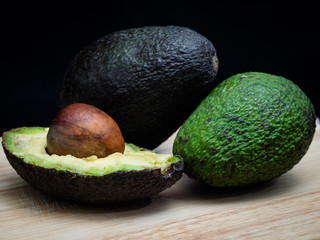 Aguacates sobre tabla de madera y fondo negro.