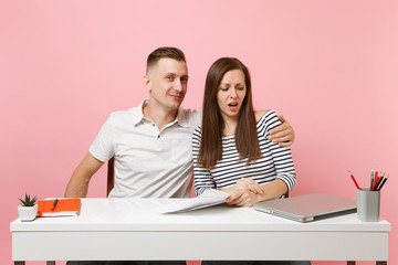 Two young business woman man colleagues sit at white desk isolated on pastel pink background....