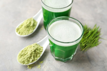 Glasses of fresh wheat grass juice and spoons with powder on grey background