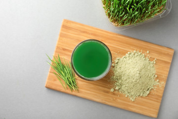 Glass of fresh wheat grass juice and powder on wooden board, top view