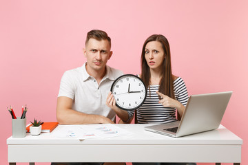 Two young fun shocked business woman man colleagues sit work at white desk with clock, laptop...