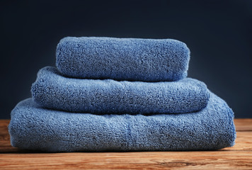 Stack of clean soft towels on wooden table against color background