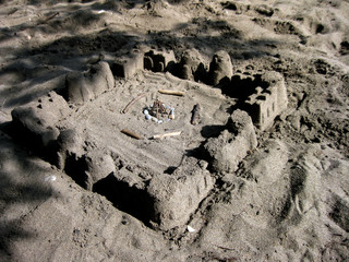 A sand fort at the beach with logs for sitting around the campfire.
