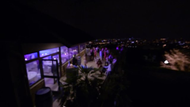 Happy dancing bride exit to the outdoor terrace on the skyscraper roof with guests applauding her and magic megapolis in the background - defocused view elevated from still drone