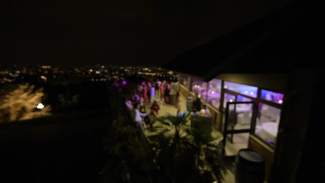 Elevated view from still drone of the happy dancing bride exit to the outdoor terrace on the skyscraper roof with guests applauding her and magic megapolis in the background - defocused view