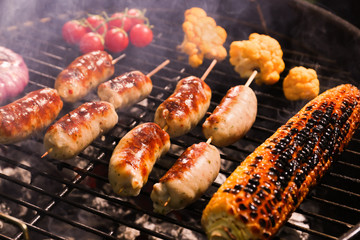 Cooking of tasty sausages and vegetables on barbecue grill, closeup
