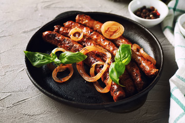 Frying pan with tasty grilled sausages and onion on table