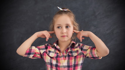 Little girl closed ears with fingers on grey background
