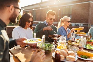 leisure and people concept - happy friends eating and drinking at barbecue party on rooftop in...