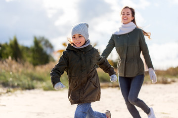 family, leisure and people concept - happy mother and little daughter running along autumn beach