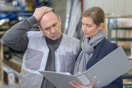 man frowning while looking at folder held by woman