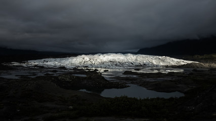 Matanuska Glacier lit up by sunlight on a dark evening.